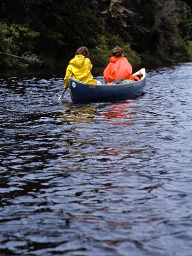 the Heathers heads down river with raincoats on the Allagash Wilderness Waterway in northern Maine