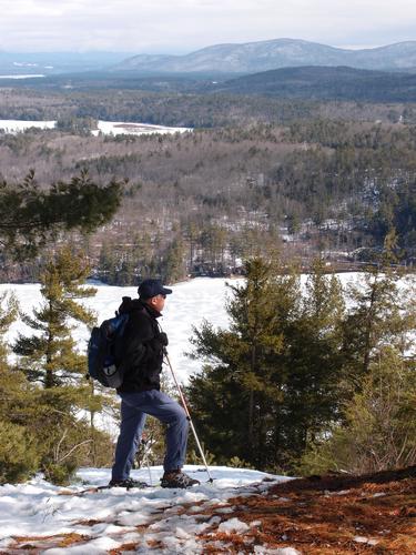winter hiker and view east over Winona Lake toward Red Hill from Bald Ledge in New Hampshire