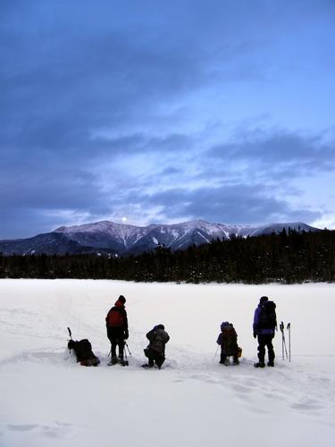 winter hikers watch moonrise over Mount Lafayette from Lonesome Lake in New Hampshire