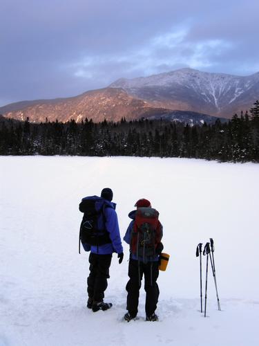 winter hikers watch sunglow on Mount Lafayette from Lonesome Lake in New Hampshire