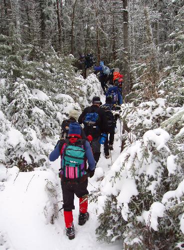 hikers in December ascend a snowy Crescent Ridge Trail to Mount Crescent in New Hampshire