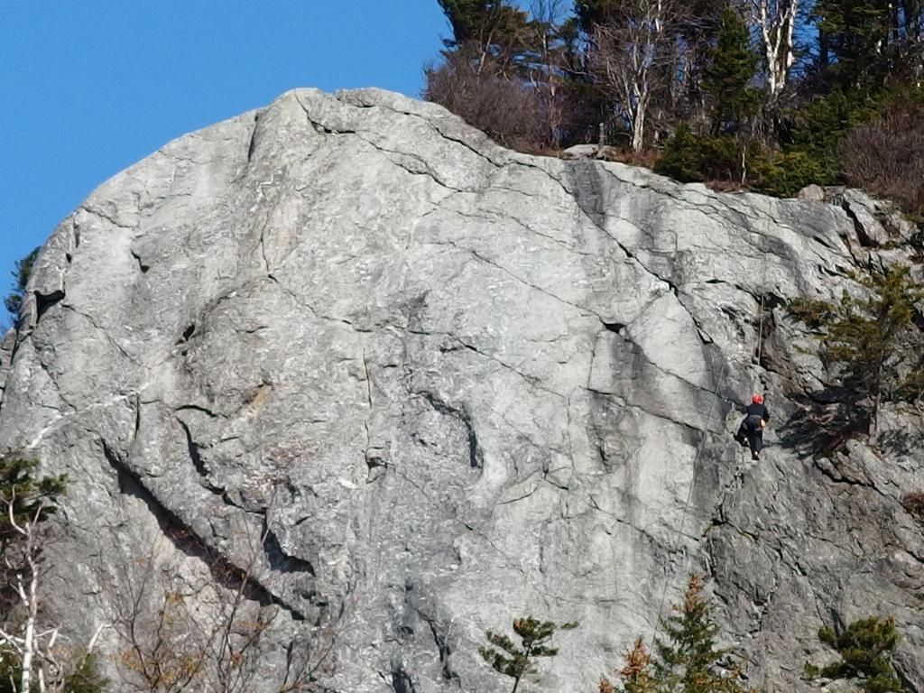 A rock climber ascends Deer Leap Rock in southern Vermont as seen from the trailhead parking lot.