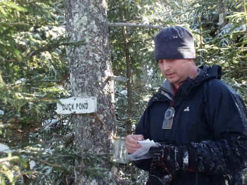 a winter hiker checks the canister log on Duck Pond Peak in New Hampshire