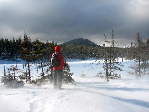 a winter hiker stands before Nancy Pond in New Hampshire