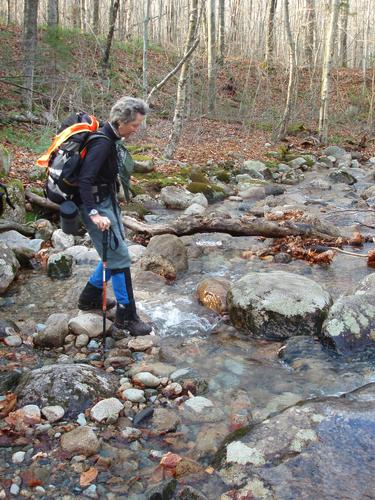 hiker crossing a stream on the trail to Mount Garfield in New Hampshire