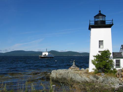 ferry approaching Islesboro island lighthouse in Maine with Camden Hills in the background across Penobscot Bay