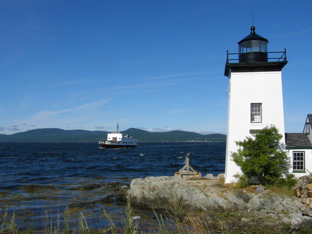 ferry approaching Islesboro Island lighthouse in Maine with Camden Hills in the background across Penobscot Bay