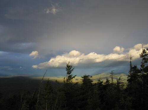 a ray from the setting sun temporarily illuminates a low-flying cloud as seen from Mount Israel in the White Mountains of New Hampshire