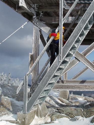 a hiker climbs the rime-coated summit tower on Kearsarge North in New Hampshire