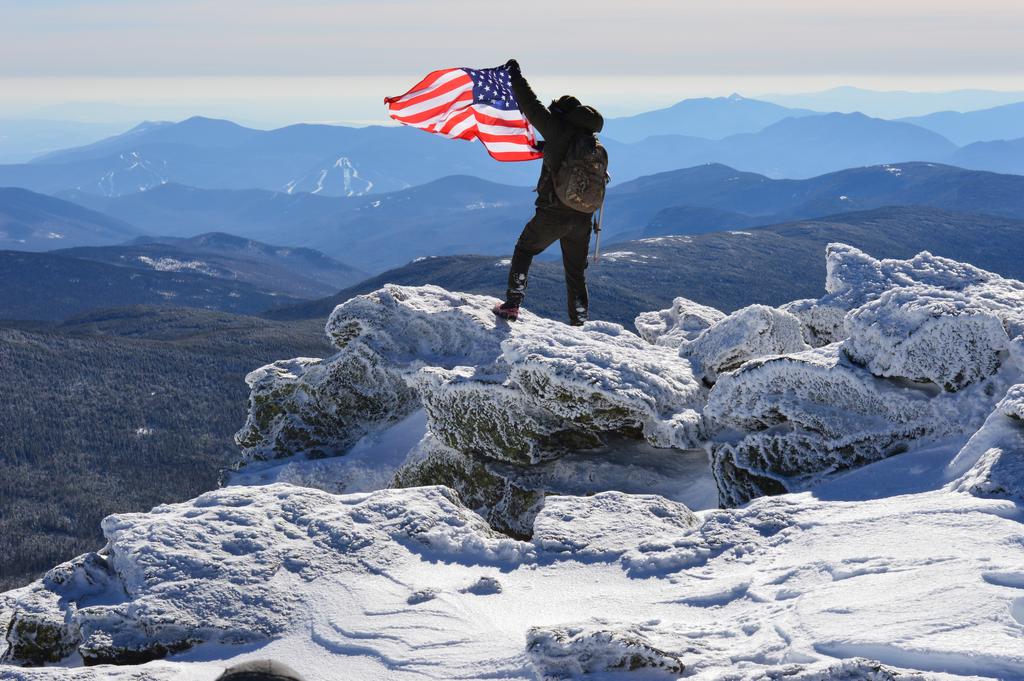 winter hiker and flag on the summit of Mount Monroe in New Hampshire