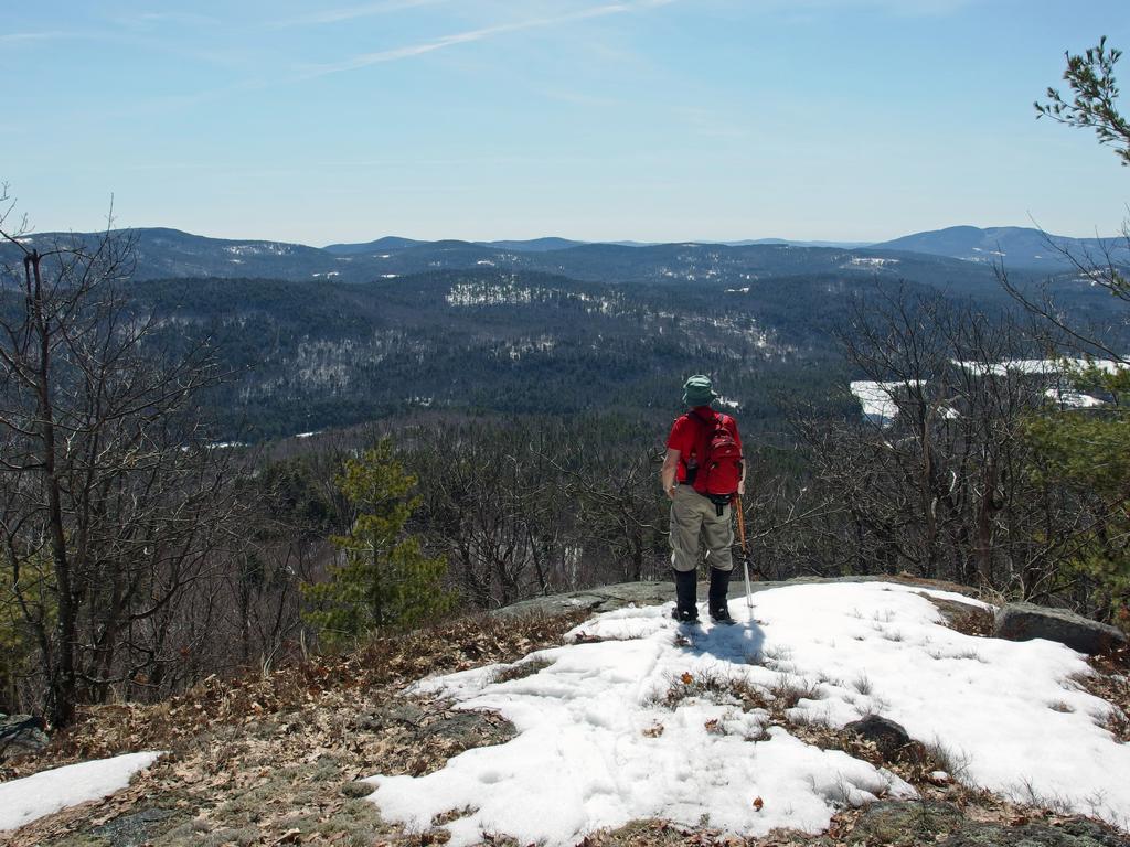 John takes in the south view in April from a ledge near the summit of Lyman Mountain in New Hampshire