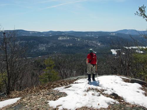 John takes in the south view in April from a ledge near the summit of Lyman Mountain in New Hampshire