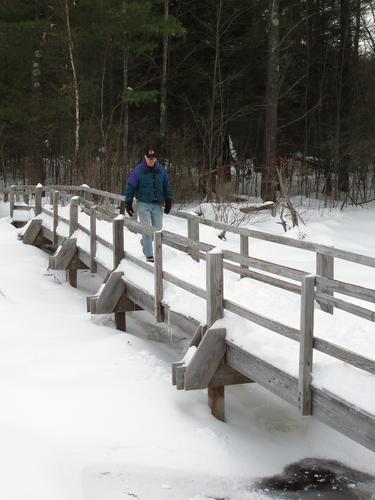 winter hiker crossing footbridge at Pond Parish Town Forest in New Hampshire