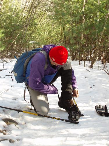 winter hiker putting on traction near Purgatory Falls in New Hampshire