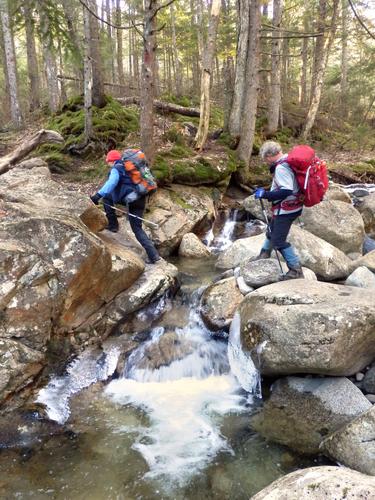 hikers crossing Rattle River on the trail to Shelburne Moriah Mountain in New Hampshire