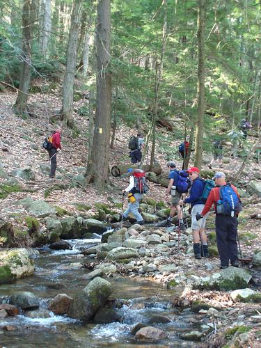 hikers cross a stream on the way to Gunstock Mountain in New Hampshire