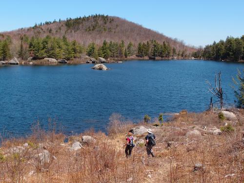 hikers at Trout Pond on the Trout-n-Bacon Trail in southwestern New Hampshire with Nancy Mountain rising on the far shore