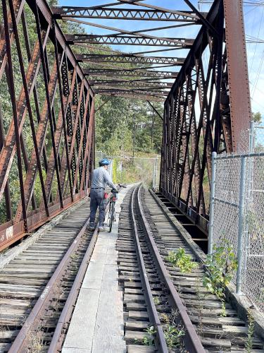John walks his bike across a bridge in October at Wayland Rail Trail near Wayland in eastern MA
