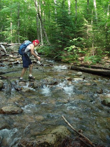 hiker crossing a stream on the Dicey's Mill Trail to Mount Passaconaway in New Hampshire