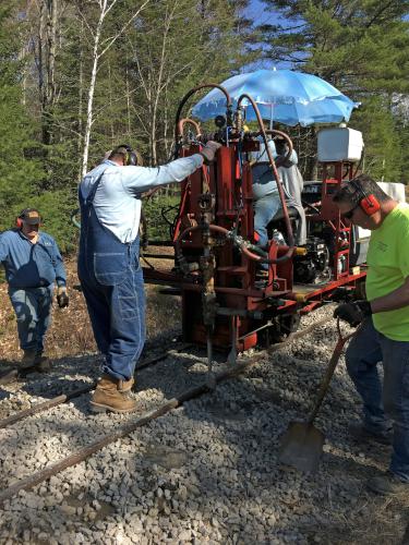 volunteers use a special machine to compact gravel between wooden ties at Wiscasset Railroad in Maine