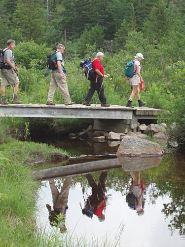 hikers cross a foot bridge on the Zealand Trail in New Hampshire