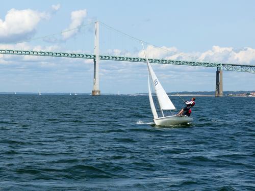 young sailors master a difficult craft, one performing a gymnastic stunt 
to counter the tipping force of the wind, at Narragansett Bay in Rhode Island