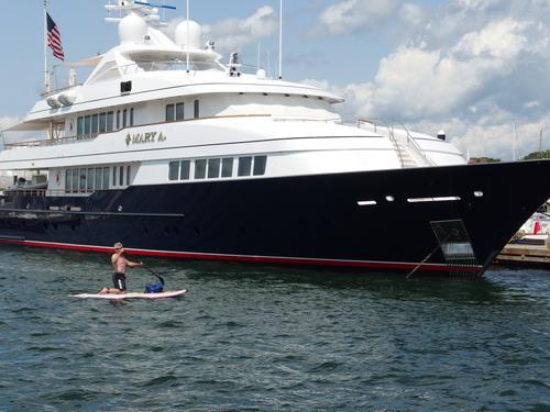 a paddler on about the smallest boat possible passes an expensive mega-boat at dock in Newport Harbor