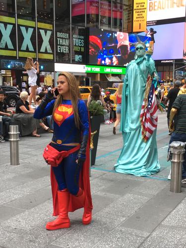 Superwoman answers her phone while the Statue of Liberty waits patiently in New York City