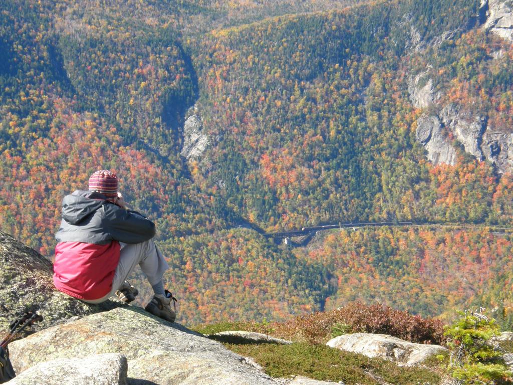 hiker photographing the tourist train across Crawford Notch from the cliffs of Mount Webster in the White Mountains of New Hampshire